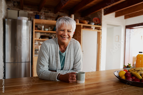 Portrait of retired biracial elderly female leaning on kitchen counter smiling at camera.