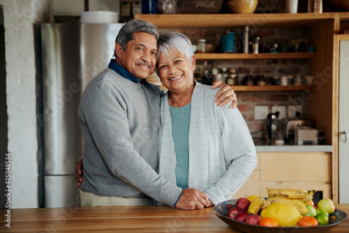 Portrait of happily retired elderly biracial couple holding each other. Healthy lifestyle, standing in modern kitchen.
