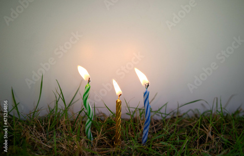 Three candles are stuck in the ground against a background of white isolate. Candles in the green grass.
