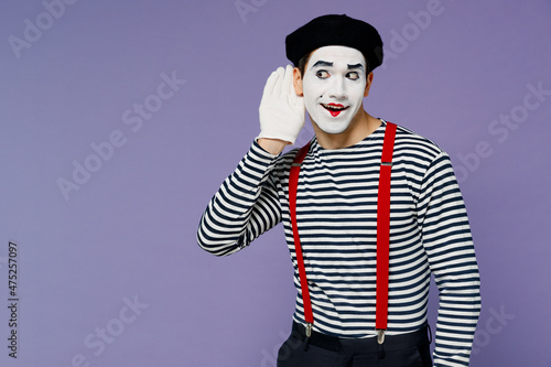 Curious nosy charismatic fun young mime man with white face mask wears striped shirt beret try to hear you overhear listening intently isolated on plain pastel light violet background studio portrait.