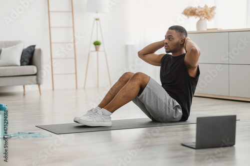 Sporty Black Man Doing Sit-Ups Exercise At Laptop Indoor, Side-View