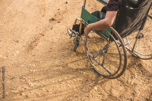 An anonymous paraplegic man on his old wheelchair with his hands resting on the handrims. Traveling on a dirt road.