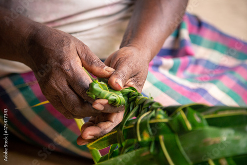 Woman weaving a coconut palm leaf into a basket for market shopping in the Solomon Islands.