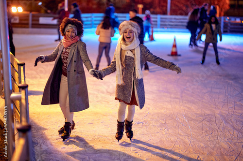 Beautiful gilfriends ice skating together; Winter joy concept