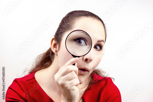 Young attractive woman with magnifying glass in her hand near the eye. Inspection, discovery, research, surprise, curiosity concept