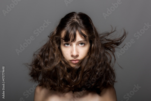 Beautiful young girl studio portrait on gray background. Looking at camera. Windy hair.