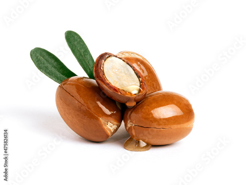  Three argan nuts with green leaves on an isolated white background. Chopped argan nut with a drop of oil. Whole and half Moroccan Argania Spinosa seeds for the production of oil