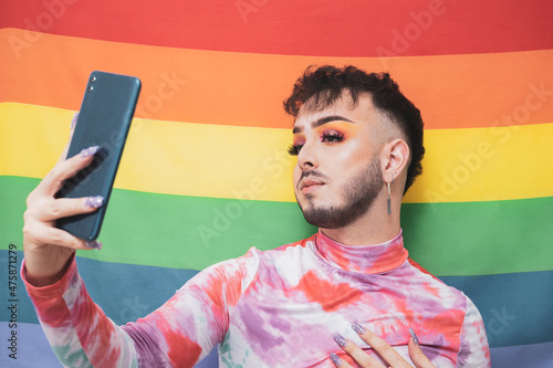 the portrait of a man with makeup taking a photo on a background of the LGBT flag.modern man concept.