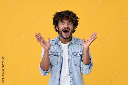 Amazed excited young indian man looking at camera with wow face expression feeling surprised advertising shopping promotion, unbelievable betting win standing isolated on yellow background.