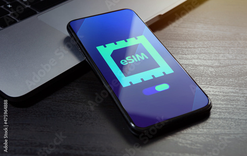 eSIM technology concept. Embedded SIM electronic phone sim card - mobile cellular global internet communication technology. Close up smartphone lying on a wooden table with an esim icon on the screen