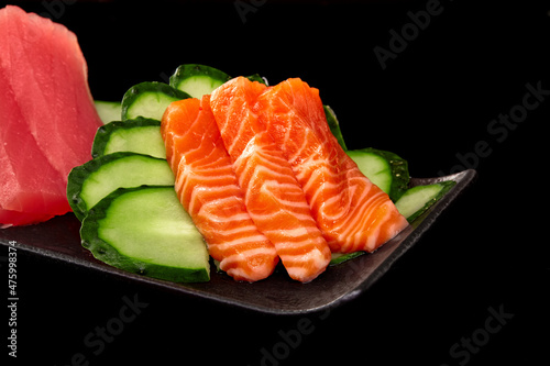 Closeup of raw salmon sashimi on platter with tuna and cucumber on black background