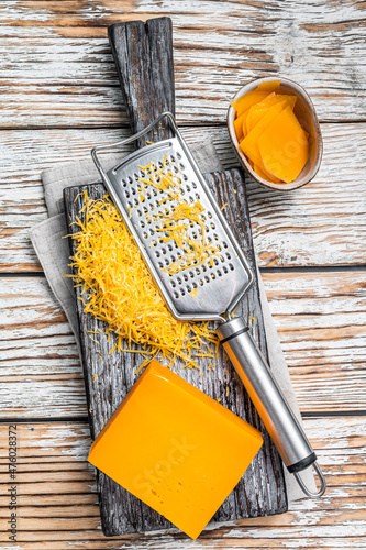 Grated Cheddar Cheese on a wooden cutting board. White wooden background. Top view