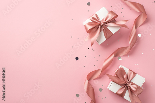 Top view photo of white gift boxes with pink bows curly ribbon silver sequins and heart shaped confetti on isolated pastel pink background with copyspace