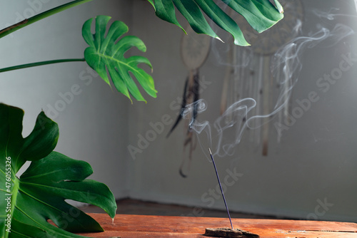 Smoke from an incense stick on the background of an interior with indoor plants and dream catchers. Meditation and mental health concept