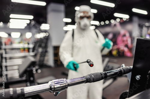 Expert warning on the serious epidemiological situation of coronavirus. Cleaning and disinfection of exercise space and gym equipment. A man in protective clothing uses a sprayer with chemicals