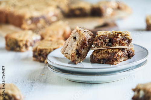 Fresh made homemade fudgy blondies or vanilla brownies stacked on a saucer over a white rustic wooden table. Extreme shallow depth of field with blurred foreground and background.