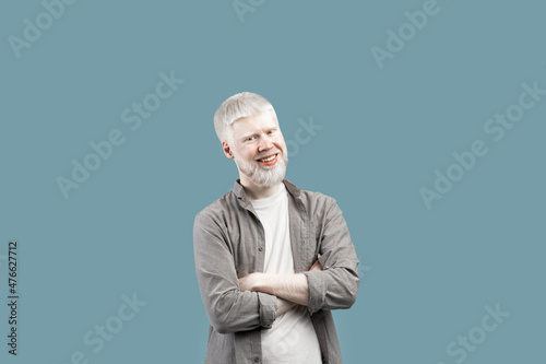 Confident person. Smiling albino guy with folded arms looking at camera, posing isolated over blue studio background