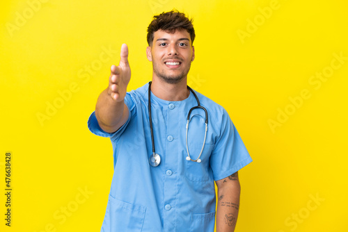 Young surgeon doctor man isolated on yellow background shaking hands for closing a good deal