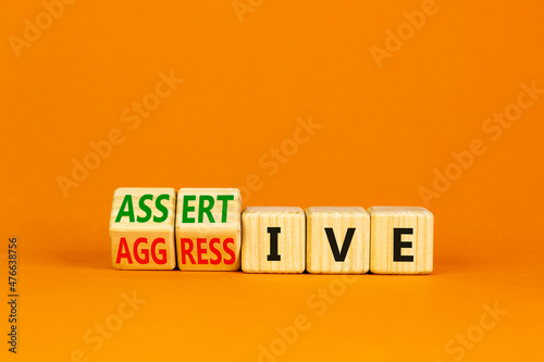 Aggressive or assertive symbol. Wooden cubes, changed the word Aggressive to Assertive. Beautiful orange background, copy space. Business, psychological aggressive assertive concept.