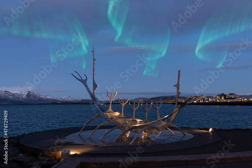 Reykjavik, Iceland. 12.22.2021. Reykjavik's symbol, the "Sun Voyager" steel sculpture against the backdrop of the city at night, snow-capped mountains and the northern lights