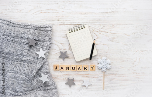 knitted sweater, letter "january", notepad, pencil, snowflake candy on white wooden background. january month calendar concept. winter season. flat lay. copy space