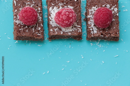 Raspberry and coconut zest on three pieces of chocolate cake. Blue background. Top view. Brownie