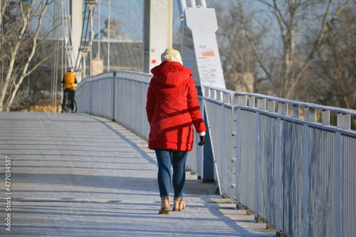 Osoba w czerwonej kurtce na Biały metalowy most zimą na niebieskim tle. 