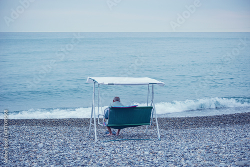 Elderly man sits in the chair by the sea.