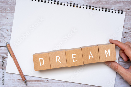 「DREAM」と書かれた積み木、ノート、ペン、人の手