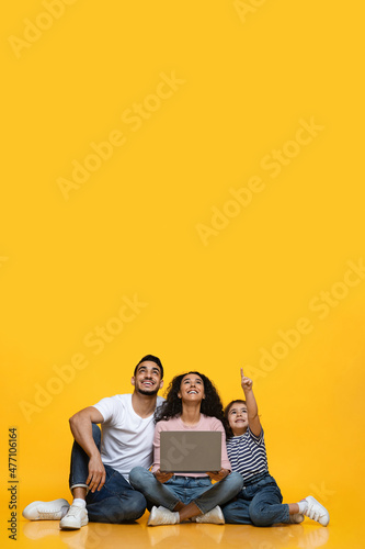 Joyful Arab Family Of Three With Laptop Pointing Up At Copy Space