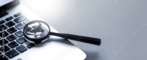 Magnifying glass put on close up of Laptop computer. Internet search concept. Wide banner or panorama.