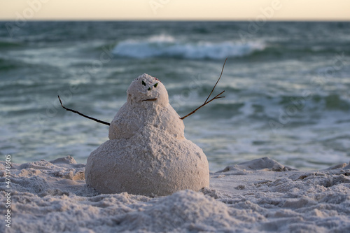 angry snowman or sandman with stick arms on the beach with oceans waves behind