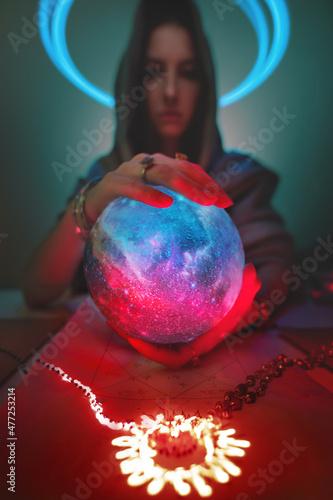 Predictable Caucasian woman with globe planet in her hands and luminous pictogram on the table. Astrology applied magic and mysticism. Focus on the texture of the ball. Clairvoyant out of focus