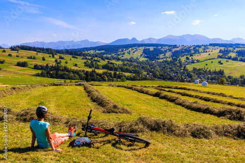Young woman sitting on meadow with bike and looking at beautiful panorama of Tatra Mountains, Poland