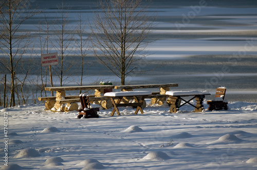 Stoły i ławki na śniegu nad brzegiem zamarzniętego jeziora