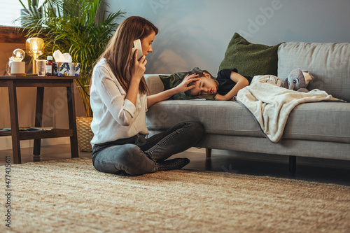 Sick boy with thermometer laying in bed and mother hand taking temperature. Mother checking temperature of her sick son. Sick child with fever and illness in bed. 