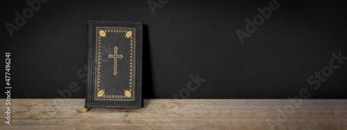 Church faith Christian background banner panorama - Old holy bible with golden cross on old rustic vintage wooden table and black wall