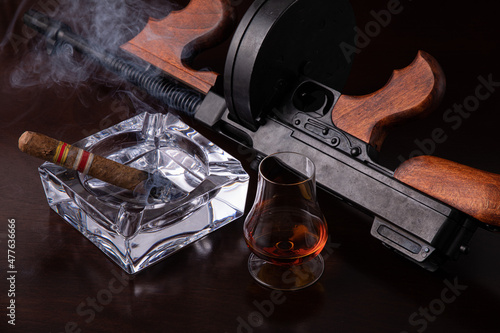 Vintage Thompson submachine gun on a dark brown table with a cigar and whiskey