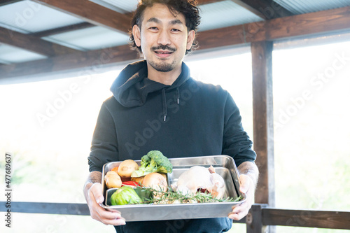 A photo of an Asian (Japanese) man showing vegetables and birds from his farm, looking at the camera.