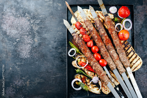 Traditional Turk Adana kebap on shashlik skewer with barbecue vegetable and flatbread served as top view on a rustic metal tray with copy space left