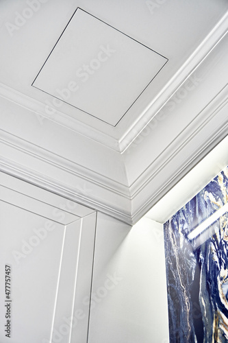 Part of elegant ceiling with LED backlight behind crown molding and small inspection hatch over blue marble wall in bathroom closeup low angle shot