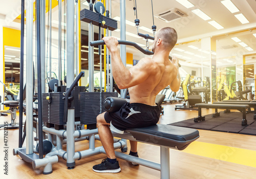 Fitness muscular man with naked torso working out in lat pulldown exercise machine in gym