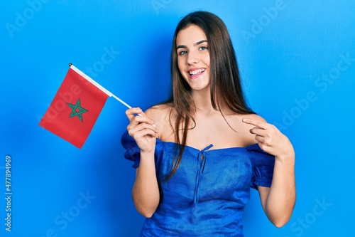 Young brunette teenager holding morocco flag smiling happy pointing with hand and finger