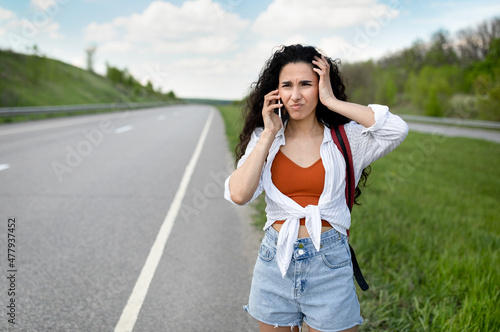 Confused young woman standing along road, feeling lost, calling on smartphone, checking travel options outdoors