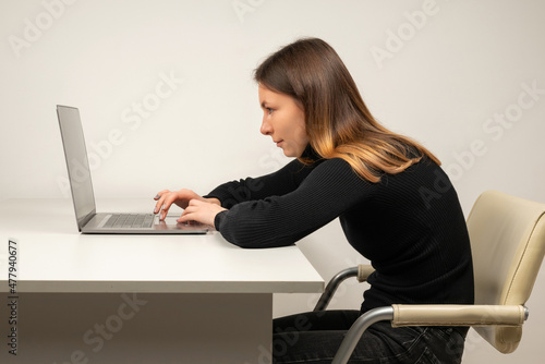 Young woman in slouching position sitting in office room, working with laptop