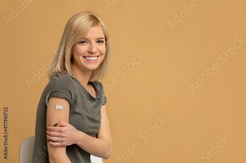 Coronavirus vaccination advertisement. Happy vaccinated lady showing arm with plaster after covid-19 vaccine injection