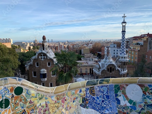 Famous colourful ceramic tiles benches at Park Guell. Panoramic view of the entrance. Skyline of Barcelona in the background. Unesco world heritage. Barcelona, Catalonia, Spain 