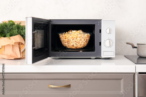 Modern microwave oven with bowl of popcorn on counter near light wall