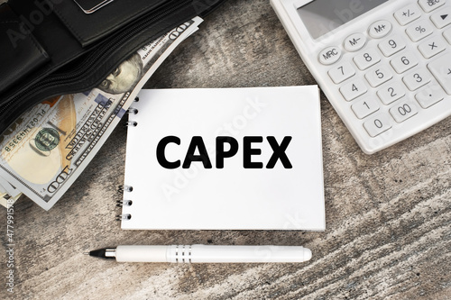 Capex is written on a white card. White calculator and black wallet with dollars on the table.