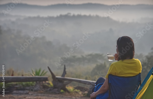 A girl is sitting and drinking in a camp with blur foggy forest background in a morning